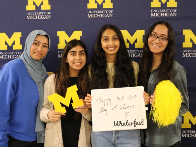 group of four students posing cheerfully in front of block m backdrop
