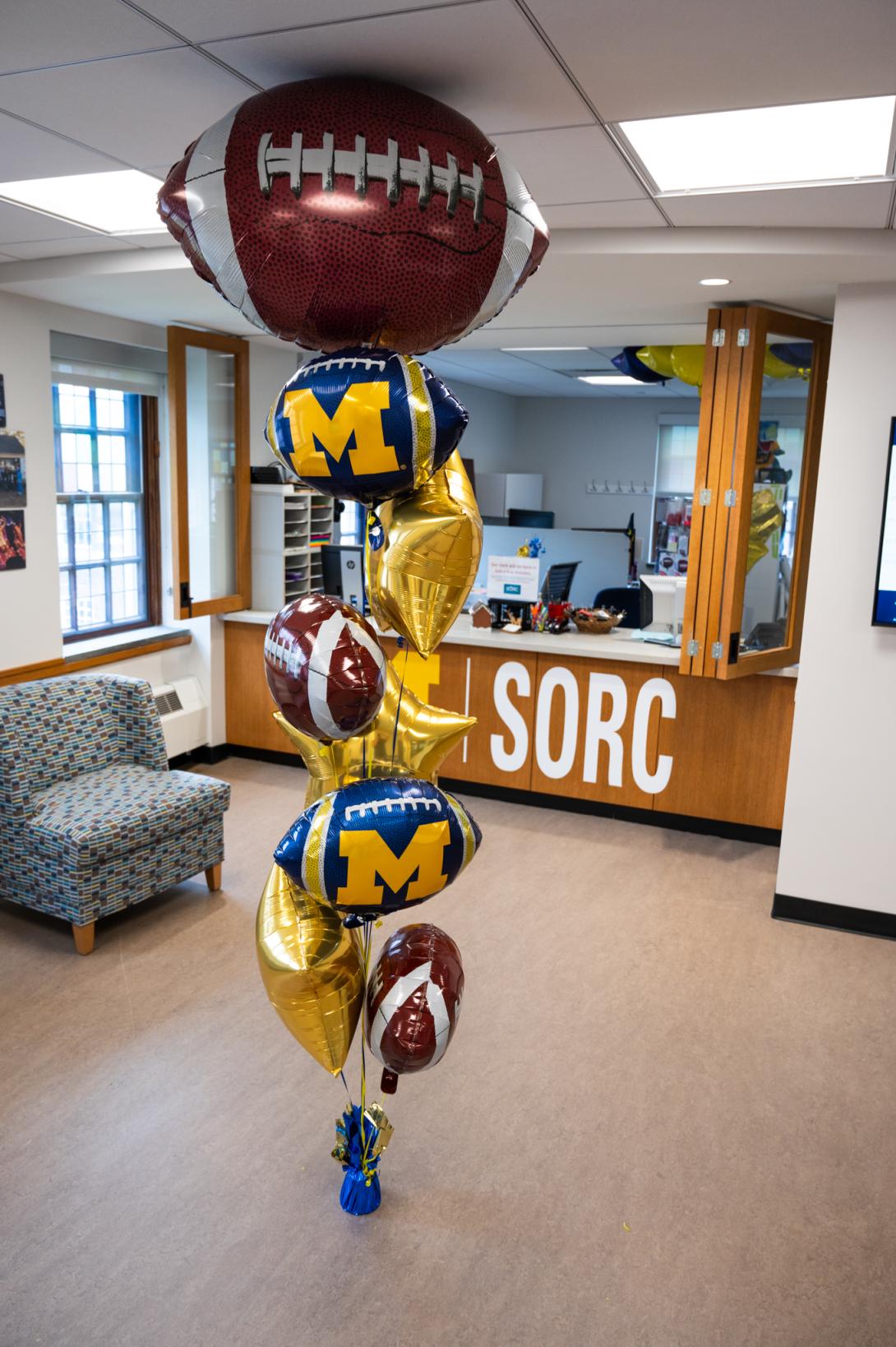 Balloon bouquet with large football on top, and then alternating smaller footballs, U of M footballs, and gold stars